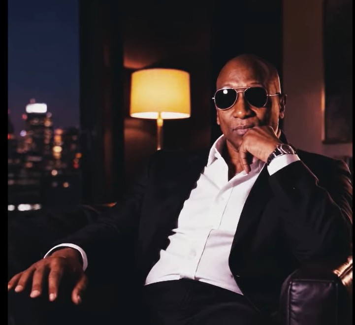Anthony Llewellyn seated in a black suit and sunglasses